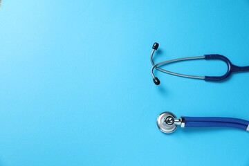 Stethoscope on light blue background, top view. Space for text