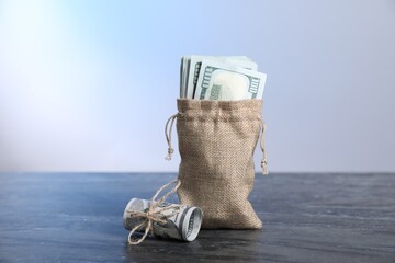 Burlap sack with dollar banknotes on grey table