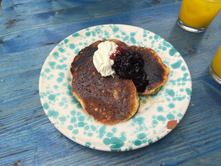 Fluffy pancakes topped with whipped cream and berry compote on a speckled plate. The vibrant toppings contrast with the rustic, blue wooden table, creating a cozy brunch vibe.