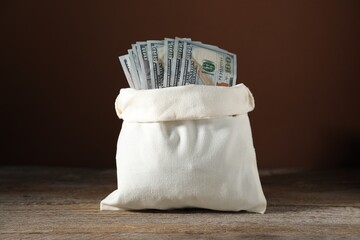 Dollar banknotes in burlap sack on wooden table against brown background