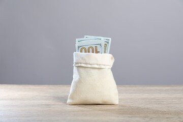 Dollar banknotes in burlap sack on wooden table against grey background