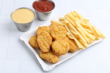 Tasty chicken nuggets and french fries with sauce on white tiled table, closeup