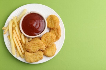 Tasty chicken nuggets and french fries with sauce on green background, top view. Space for text