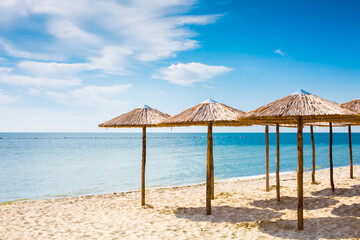 Row of wooden umbrellas at sandy beach, sea and blue sky