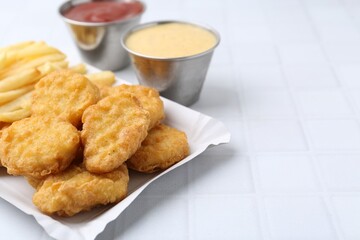 Tasty chicken nuggets and french fries with sauce on white tiled table, closeup. Space for text