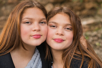 Two twin sisters with long brown hair hugging and smiling