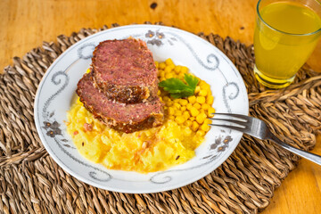 Meatloaf, mashed potato and corn on plate, fork, juice on bamboo pad.