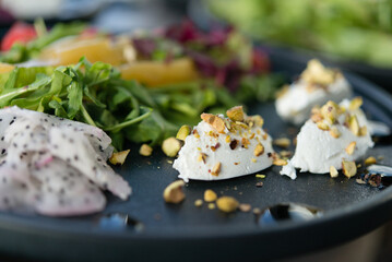 soft cheese quenelle, sprinkled with chopped pistachios and salad greens, served on a black platter