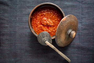 Spicy red hot chili sauce in clay bowl with a wooden spoon and dark background