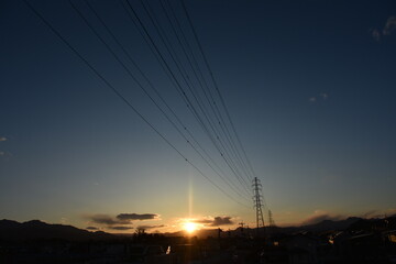 夕暮れ時の山の向こうに見える送電線と鉄塔