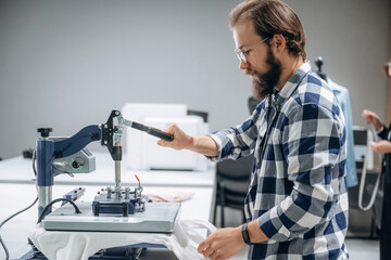 Guy in checkered shirt is working. People are by the sewing machines indoors