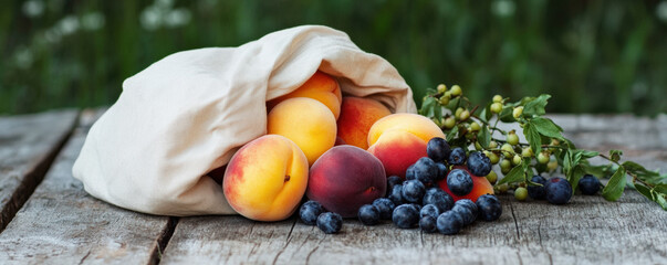 Fresh peaches and blueberries in reusable fabric bag on wooden table, surrounded by greenery. This vibrant scene captures essence of summer and healthy eating