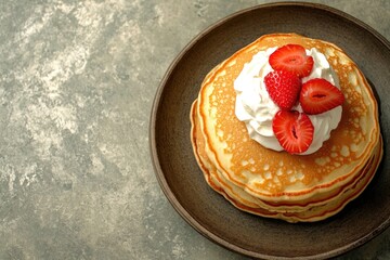Fluffy pancakes topped with whipped cream and fresh strawberries
