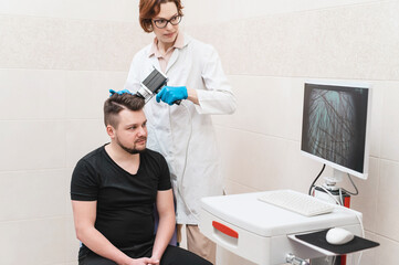 Fototapeta premium Female doctor looks at a man's scalp with a dermatoscope. Diagnosis of scalp condition by a trichologist. Mole examination, baldness, hair transplantation