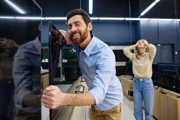 A couple is actively shopping for a new television at their local electronics store