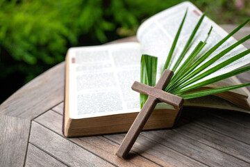 Crucifix cross and palm leaf on top of Holy Bible. Palm Sunday or Easter holiday concept.