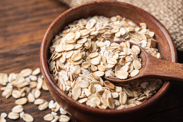 Rolled oats, oat flakes in wooden bowl on a wooden table background. Uncooked oats. Healthy diet food