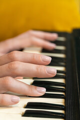 Obraz premium Close-up of female hands playing a synthesizer, creating music in a cozy home or professional studio setting with a yellow sofa in the background, evoking a creative and artistic atmosphere