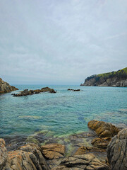 A tranquil scene of a rocky coastline with clear blue waters under a cloudy sky. the rugged rocks create a natural frame for the calm sea. sparse greenery atop cliffs adds contrast to the serene blues