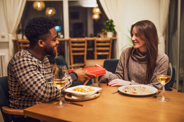 Two friends are having dinner at restaurant. They are exchanging gifts.