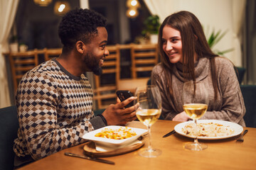 Two friends are having dinner at restaurant. They are using smartphone.