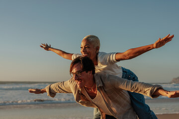 Happy couple playing airplane on beach at sunset
