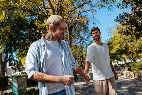 Gay couple holding hands and walking in a city park - Powered by Adobe