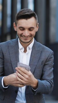 Vertical Format Video of Lifestyle, richness, joy, success. Happy rich successful man holds dollars outdoors. Portrait of satisfied businessman holds money