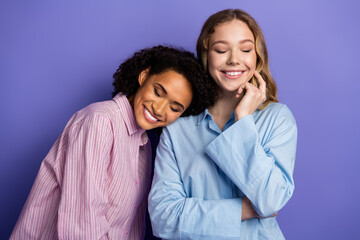 Two young women expressing happiness and friendship, resting together in stylish pajamas against a purple background