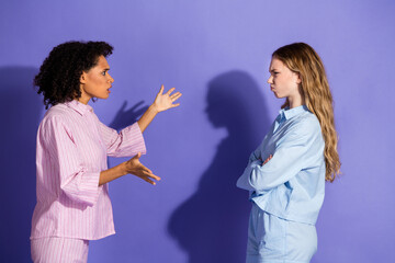 Two young women in sleepwear having an emotional discussion against a vibrant purple background,...
