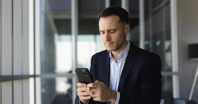 Focused serious Hispanic company director man in formal jacket using financial service on smartphone for online transactions, payment, typing on mobile phone, looking away, thinking