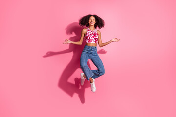 Happy young woman jumping with joy on pink background dressed in trendy top and jeans showcasing...