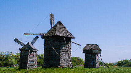 Three old wooden windmills on flat green grass against a blue sky