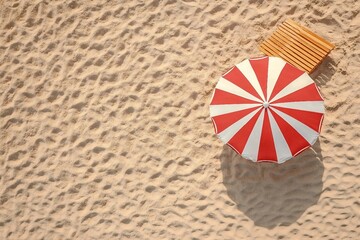 Striped beach umbrella near wooden sunbed on sandy coast, aerial view. Space for text