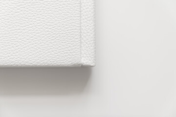 corner of book in white leather cover on white table. binding for photo album
