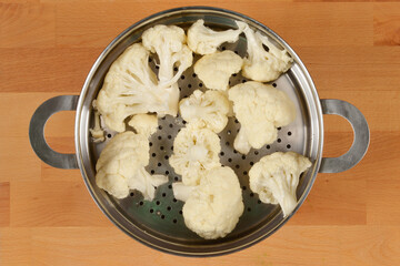A top-down view of fresh cauliflower florets in a metal steamer basket, ready for cooking
