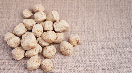 The image showcases a pile of soya chunks, also known as textured vegetable protein (TVP). The chunks are small, round, and have a light brown color. They appear porous and slightly textured
