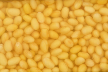 A close-up, high-angle shot of soybeans soaked overnight, showcasing their plump texture and hydrated appearance in a clear liquid