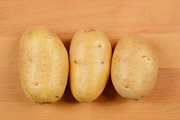 A close-up, top-down shot of three whole potatoes on a wooden surface, showcasing their natural texture and color