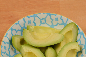 A close-up shot of ripe avocado slices in a decorative bowl against a light wooden background