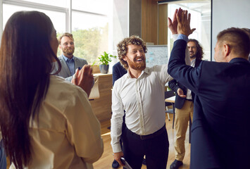 Happy, smiling business mentor gives high five to young man. Team of corporate employees having fun...