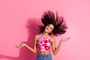 Joyful young woman with curly black hair wearing a printed top, posing against a stylish pink backdrop showcasing youthful charm.