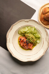 Sliced smoked salmon arranged with mashed avocado and cucumber ribbons on a decorative plate, top view