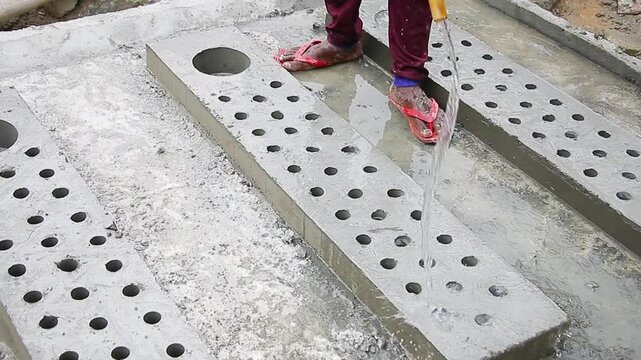 Indian mason worker pouring water on freshly poured concrete slab to increase hardening