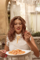 young woman eating spaghetti. she is wearing a summer white dress