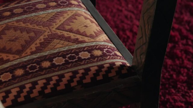 Close up of a traditional Moroccan chair with patterned upholstery and carved wooden frame. The chair sits on a deep red rug with a textured surface. cultural richness and traditional craftsmanship.