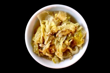 Small white bowl filled with cooked or pickled cabbage, seen from above against a dark background.