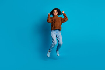 Joyful young woman in casual outfit jumping against bright blue background expressing happiness and...