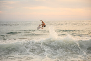 Surfer performing trick on skimboard at sunset