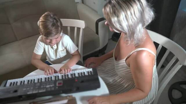 A boy plays a synthesizer piano in a music lesson at home with his mother, a music teacher